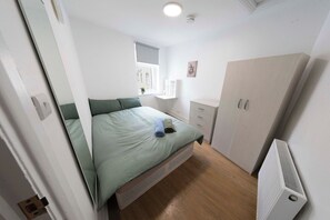 A bedroom with a bed, a bedside table, a radiator, and a wardrobe. - Spacious 4BR Home in Mile End – Amazing Location (Greater London)