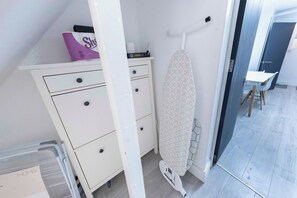 A room with a white dresser, a patterned ironing board, and a small table with a chair. - Spacious 4BR Home in Mile End – Amazing Location (Greater London)