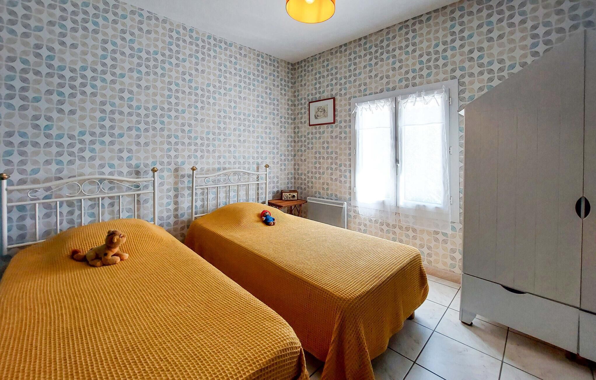Een kamer met twee bedden, een radiator, een raam met gordijnen, een kledingkast en een foto aan de muur.