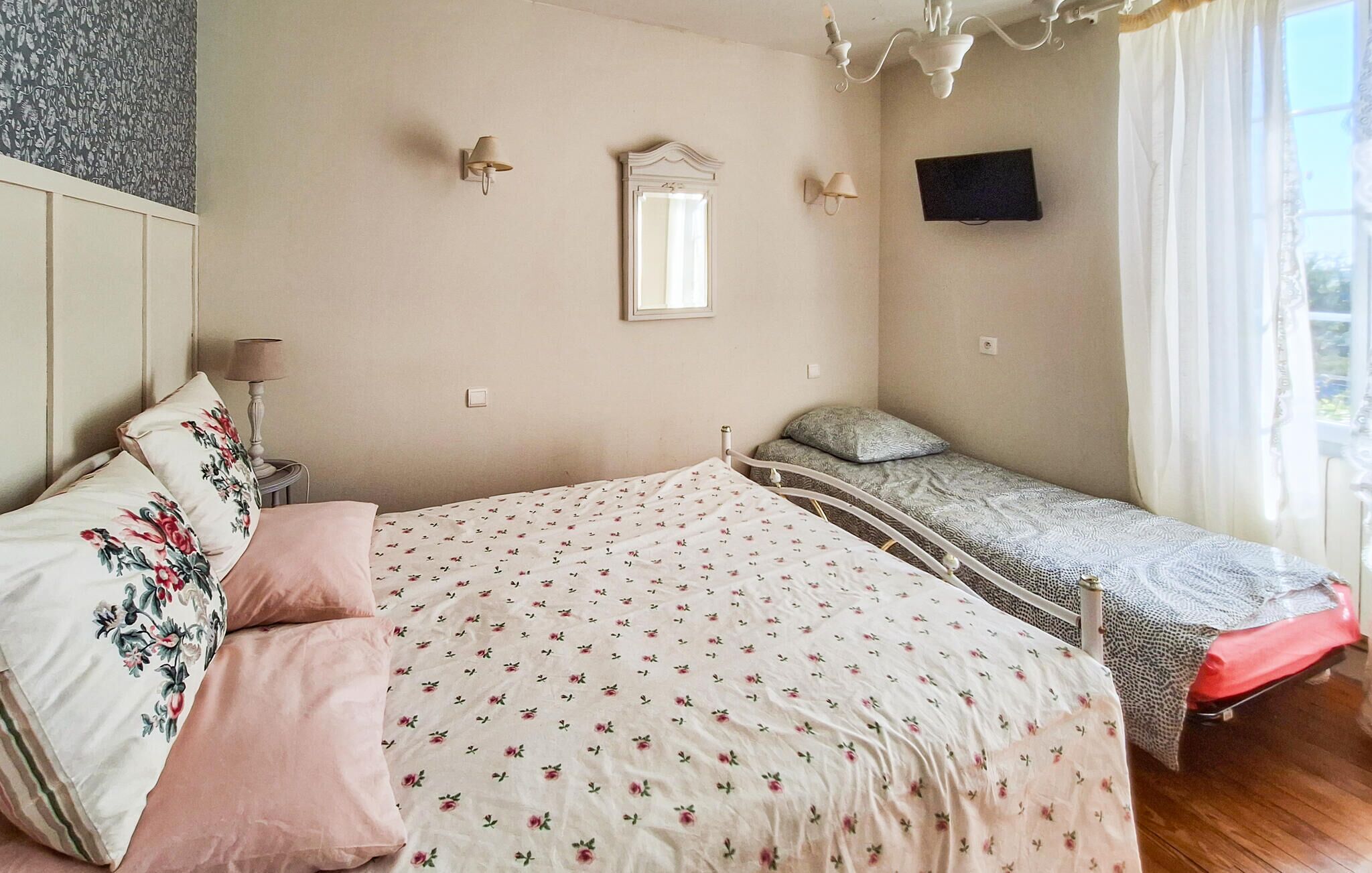 Un dormitorio con cama, mesita de noche, espejo, televisor y ventana con cortinas.