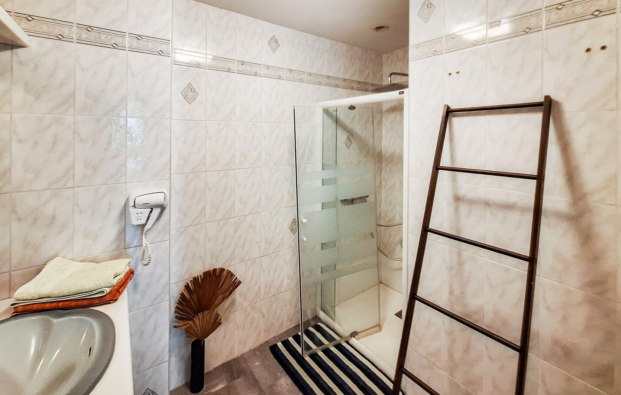A bathroom with a shower, a towel rack, a hairdryer, and a broom.