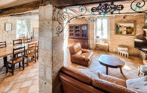 A rustic room with a wooden dining table, leather sofa, and a cabinet with glass doors. - Jolie maison avec piscine (Castet-Arrouy)