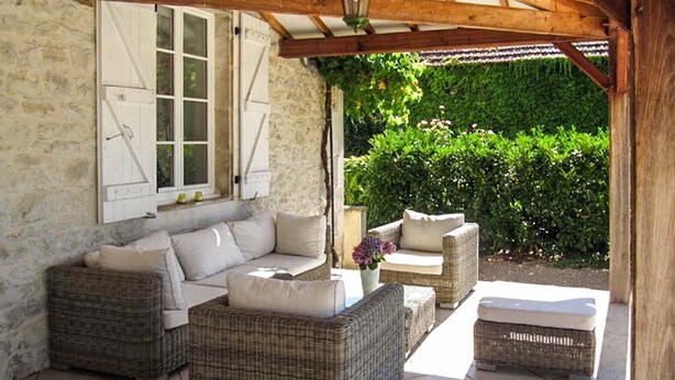 A covered patio area with wicker furniture, a stone wall, and a view of greenery. - Gorgeous home in Tauriac (Tauriac)