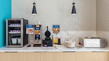 A self-service food station with yogurt, waffles, and a waffle maker.