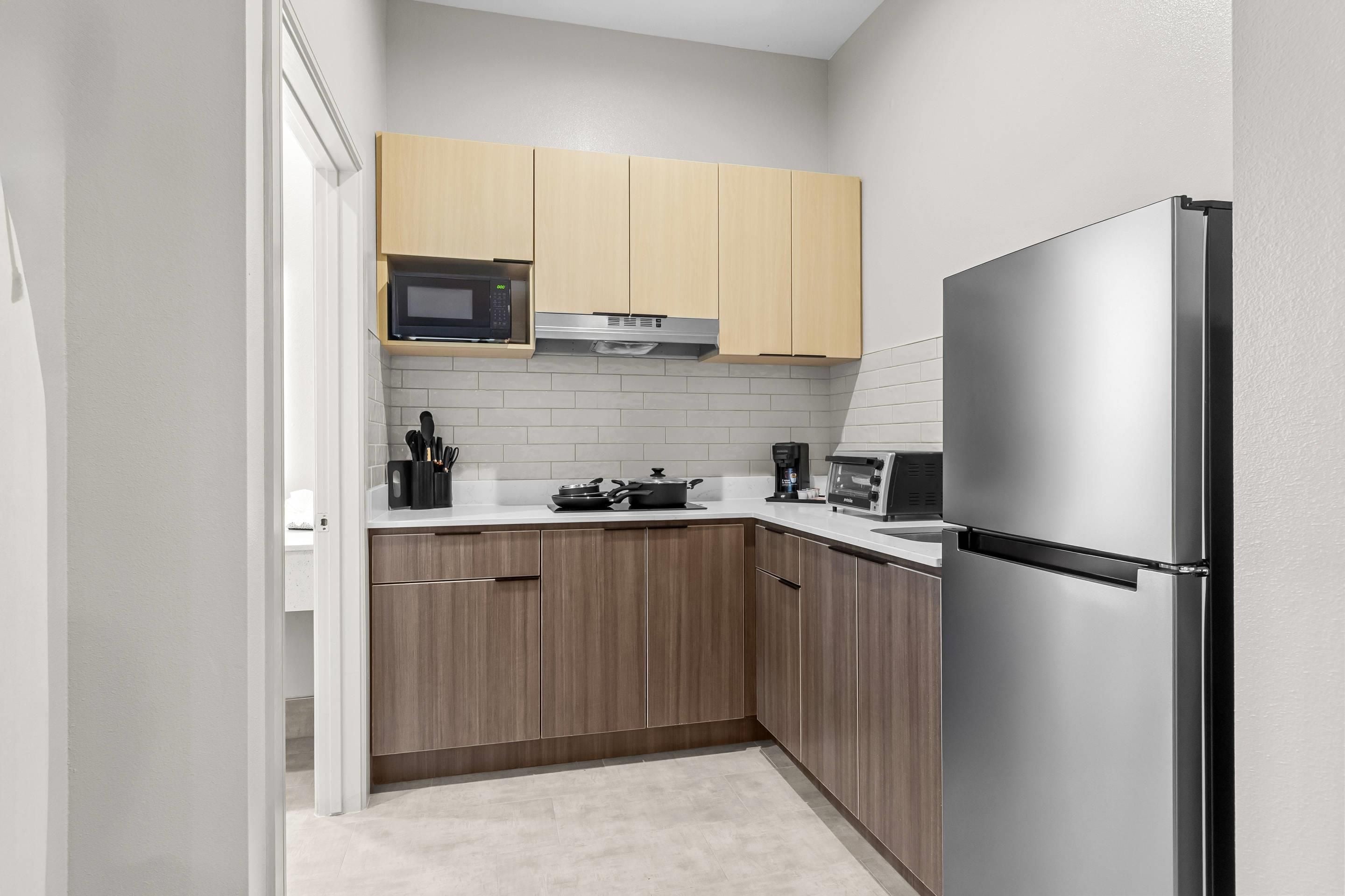 Una cocina compacta con armarios de madera, un refrigerador de acero inoxidable, un microondas y un tostador.