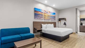 A hotel room with a bed, a blue sofa, a small table, and a wall-mounted shelf with a microwave.