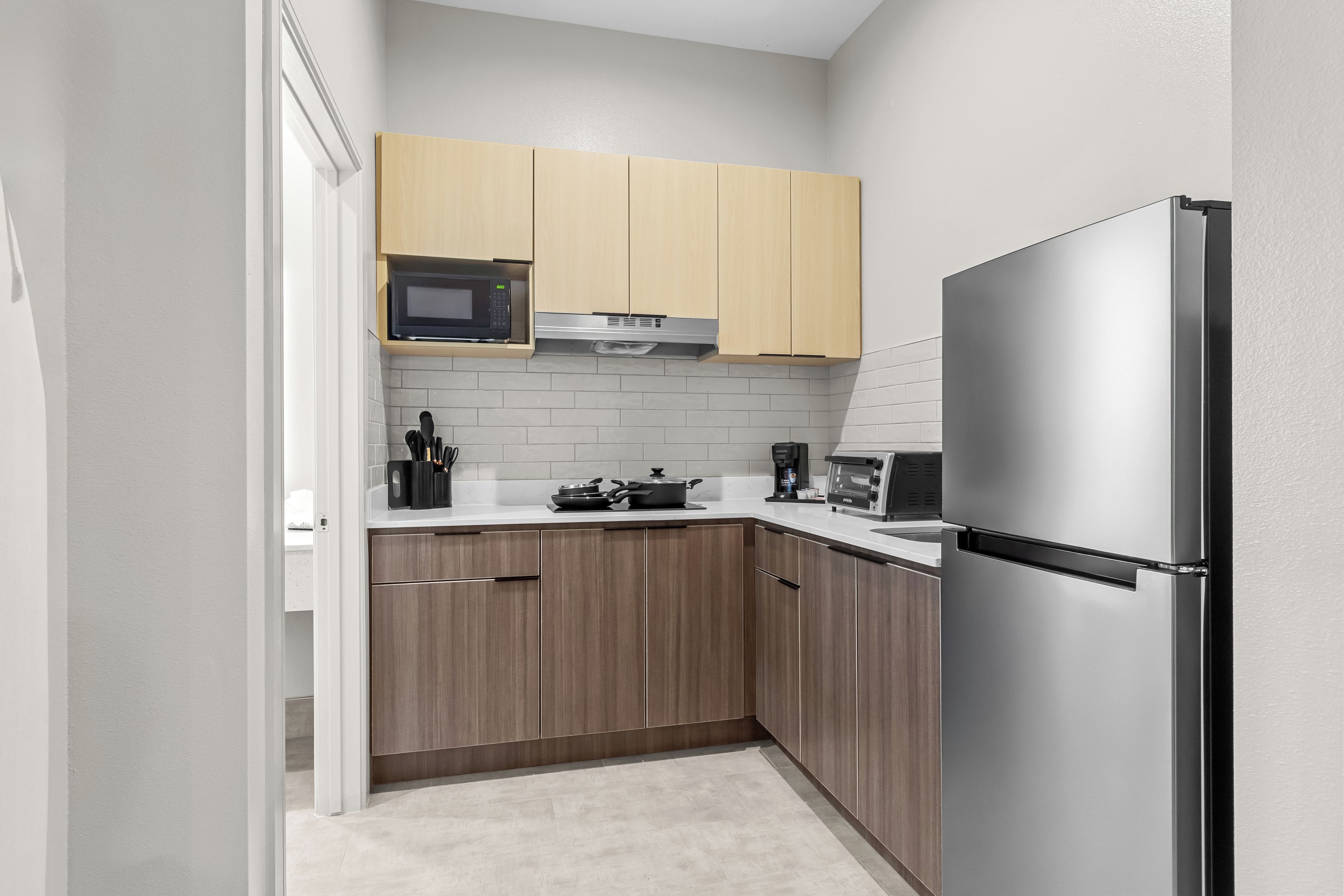 A compact kitchen with wooden cabinets, a stainless steel refrigerator, a microwave, and a toaster.