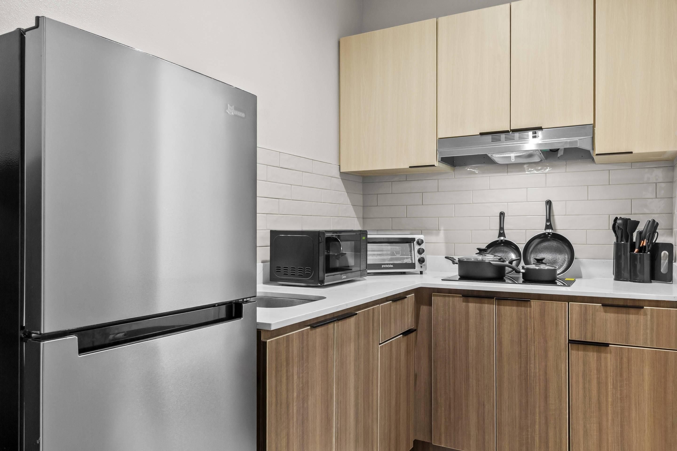 Una cocina moderna con un refrigerador de acero inoxidable, un microondas integrado, un horno tostador y una estufa con ollas y sartenes.