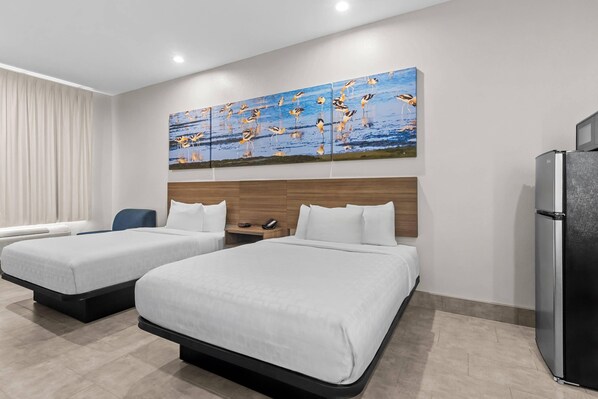 Habitación de hotel con dos camas, cabecera de madera, un refrigerador y una obra de arte con aves colgada en la pared.