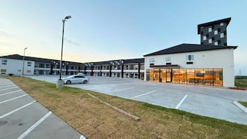 A modern building with a parking lot, a car, and a grassy area.