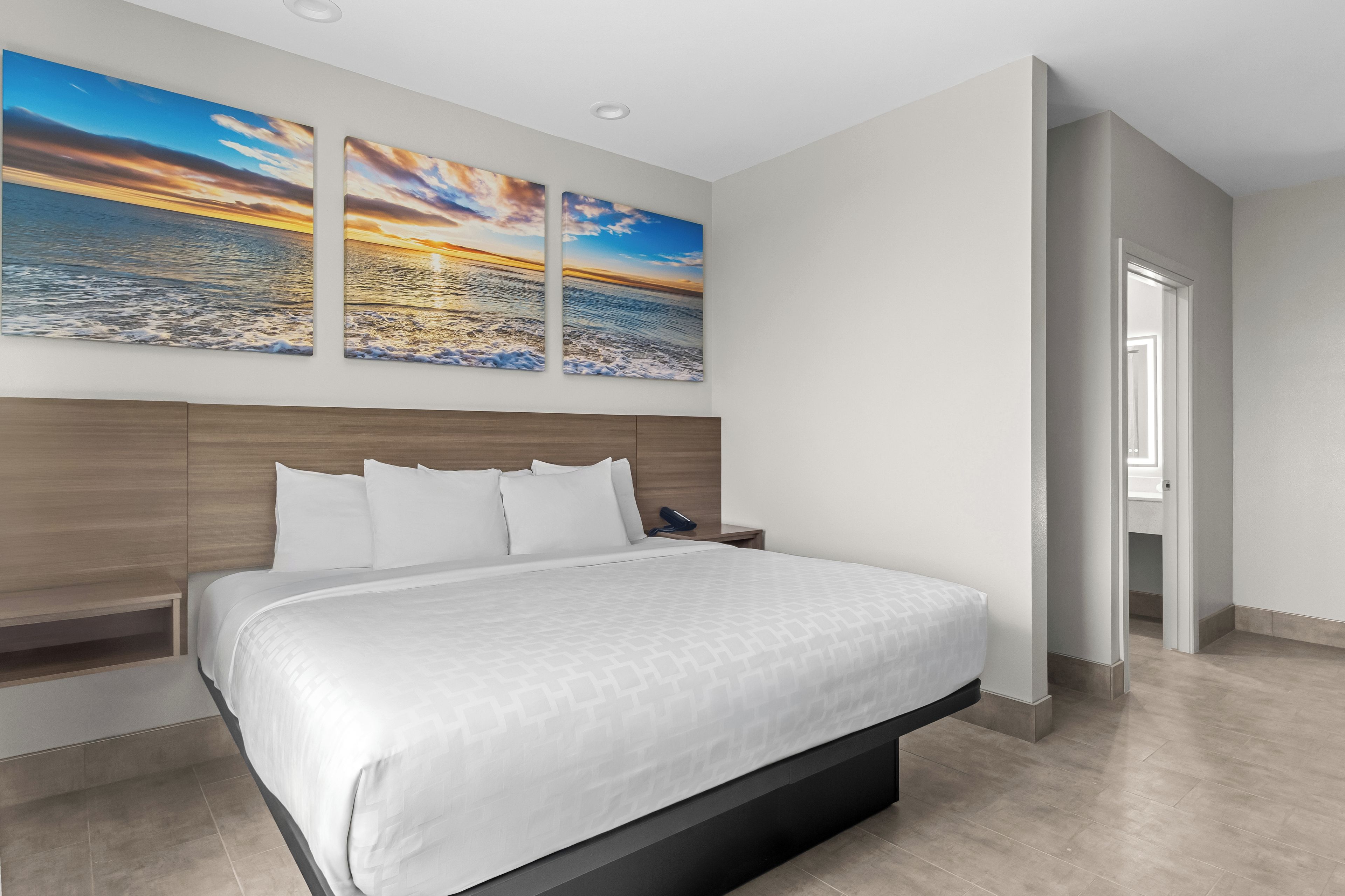A modern bedroom with a large bed, a wooden headboard, and three wall-mounted sunset paintings.
