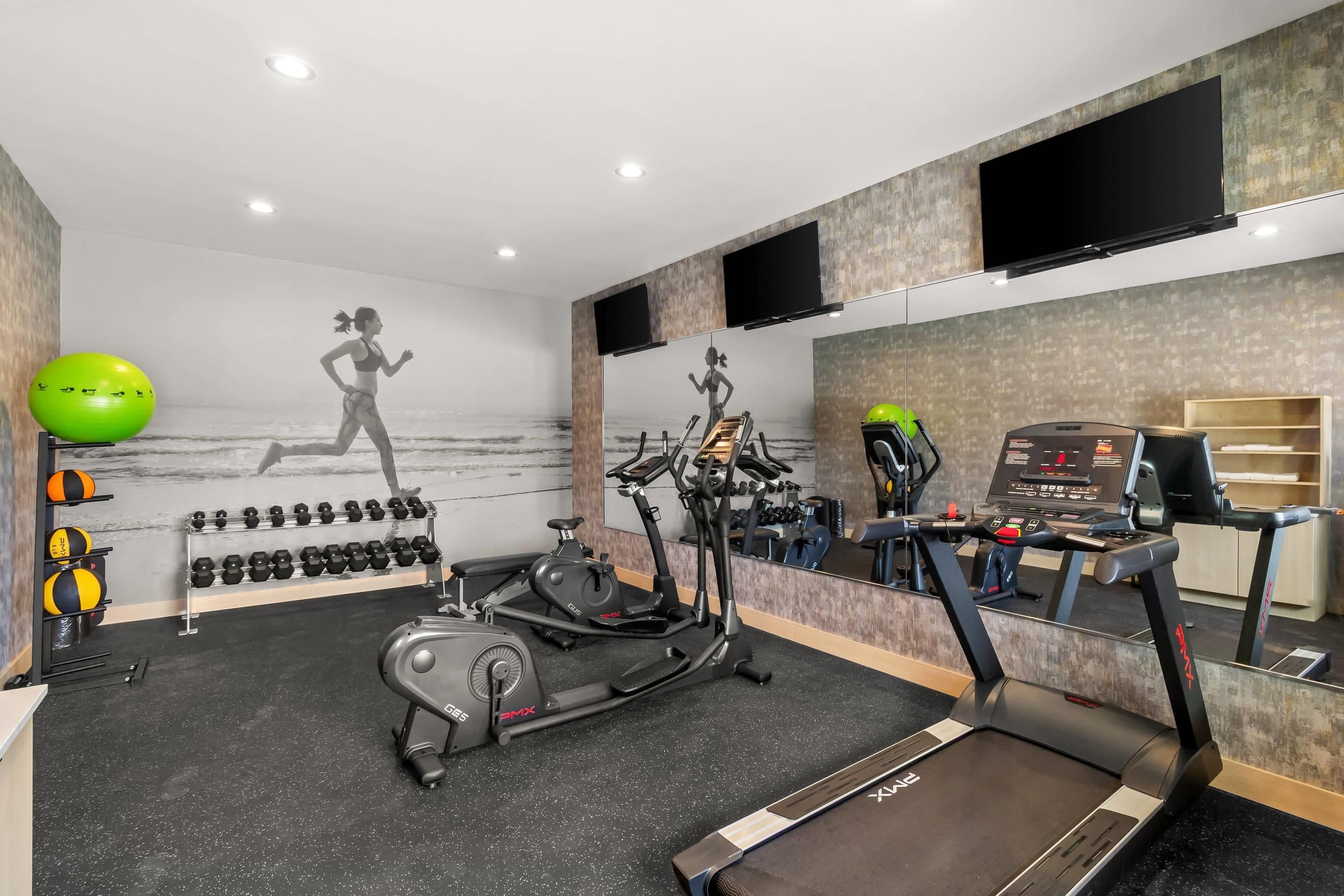 A gym with exercise equipment, a treadmill, and a wall-mounted TV.