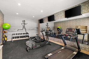 Un gimnasio con equipo de ejercicio, una cinta de correr y un televisor montado en la pared.