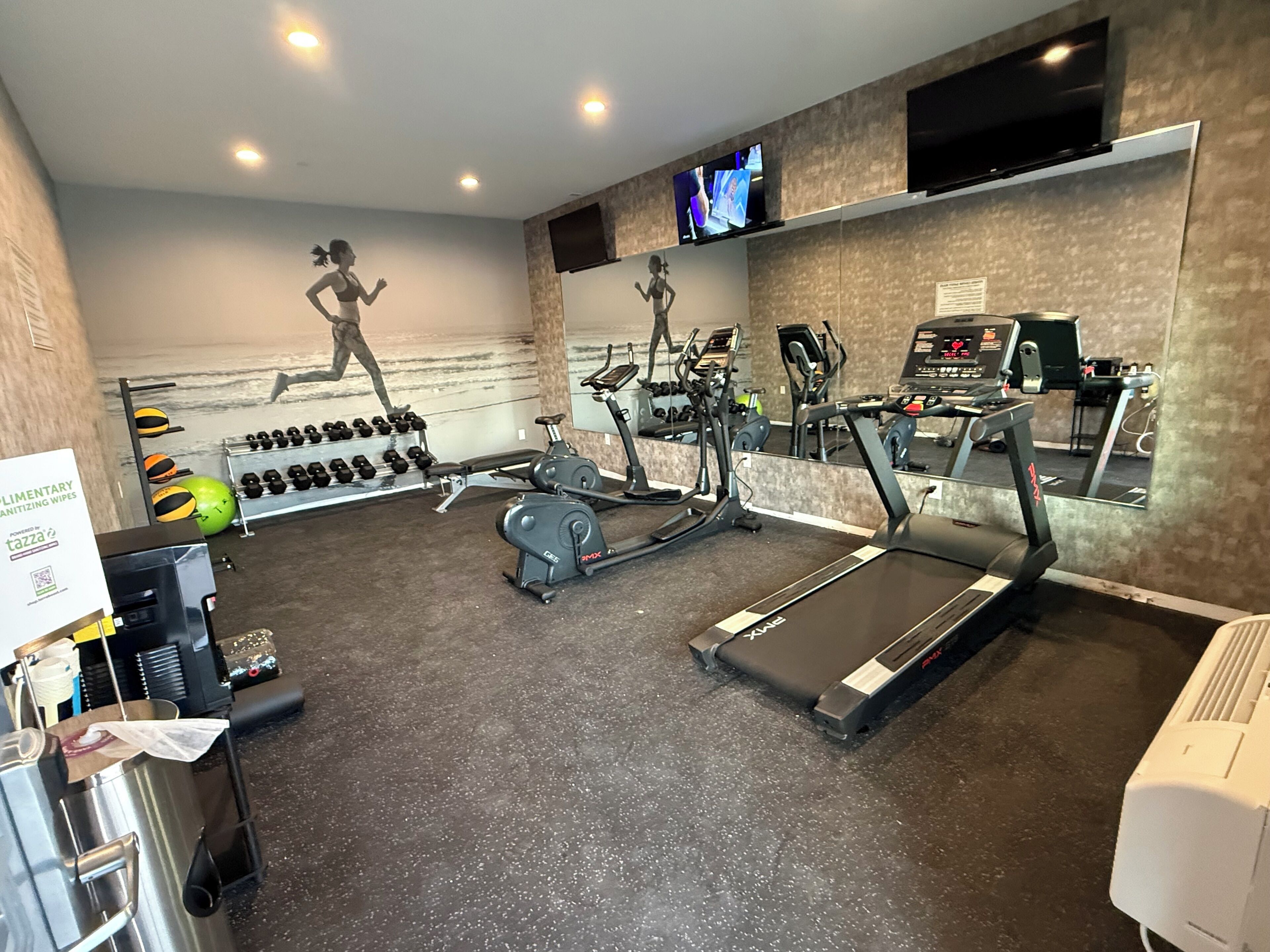 A gym with treadmills, dumbbells, and a mirrored wall.