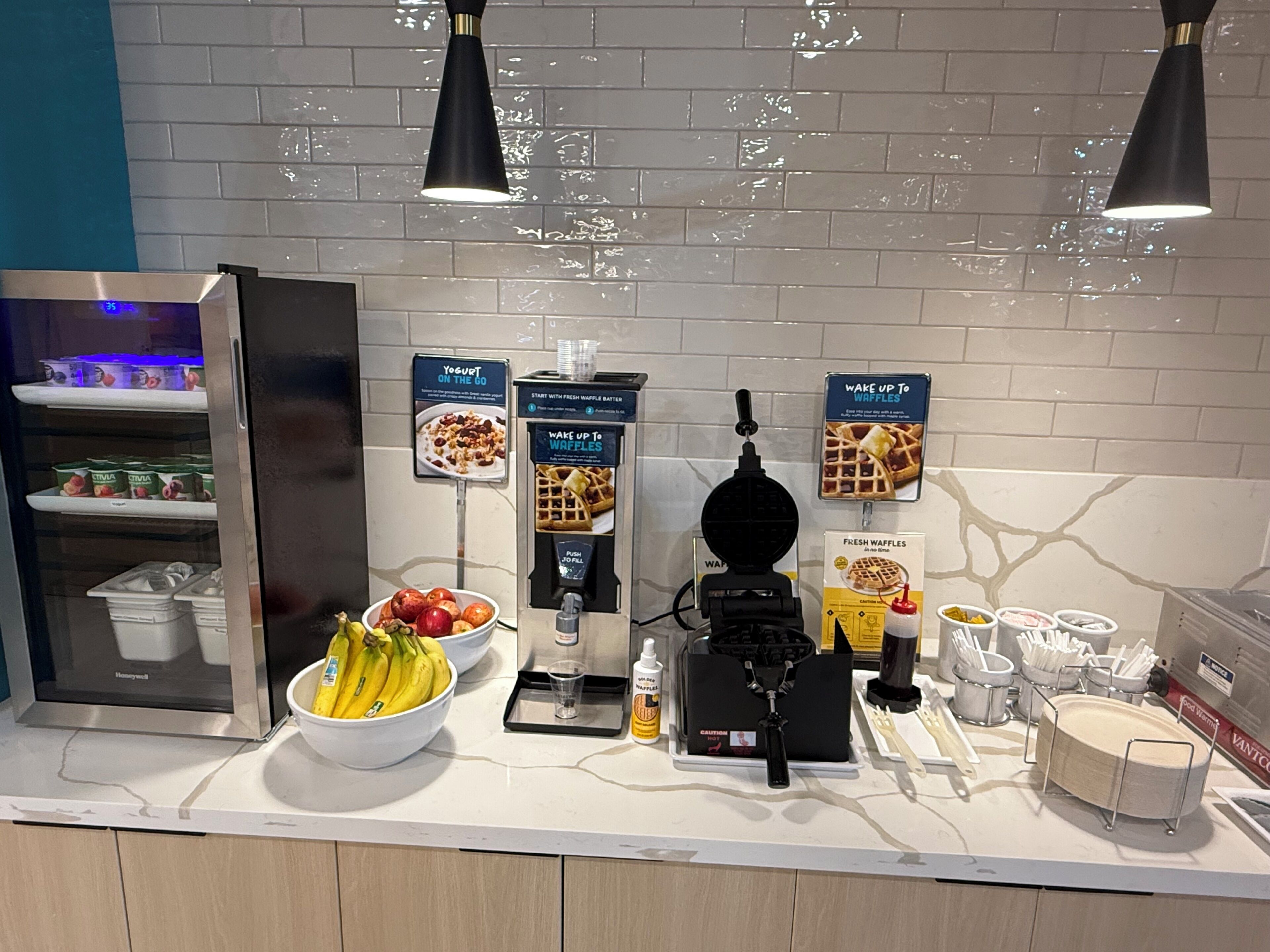 Uma mesa de café da manhã com máquina de waffle, iogurte e frutas frescas.