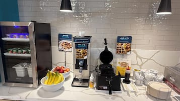 Uma mesa de café da manhã com máquina de waffle, iogurte e frutas frescas.