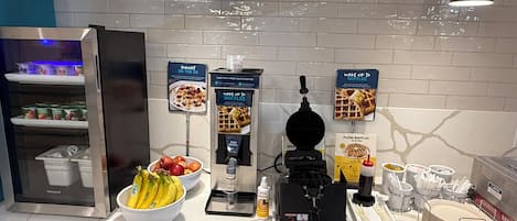 A breakfast bar with a waffle maker, yogurt, and fresh fruit.