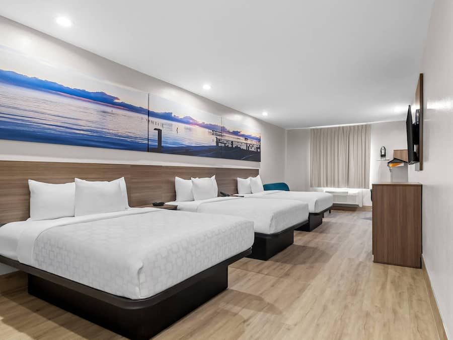 Une chambre d’hôtel avec trois lits, un bureau et une grande fenêtre.