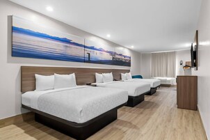 Habitación de hotel con tres camas, un escritorio y un ventanal grande.