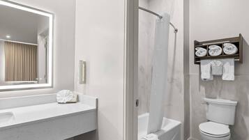 A modern bathroom with a white vanity, a large mirror, a shower enclosure, and a toilet.