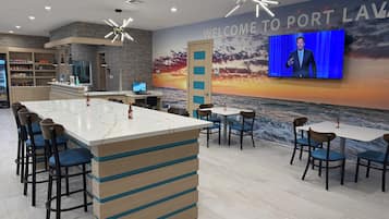 A modern bar area with a large TV screen, seating, and a wall mural depicting a sunset over the ocean.