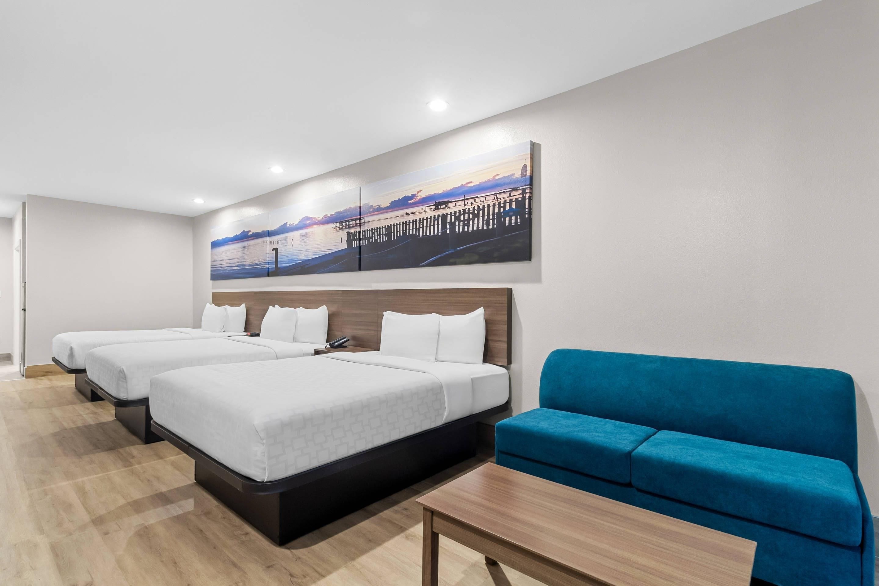 Hotellihuone, jossa on kaksi sänkyä, sohva ja maalaus, jossa on kuvattuna laituri.