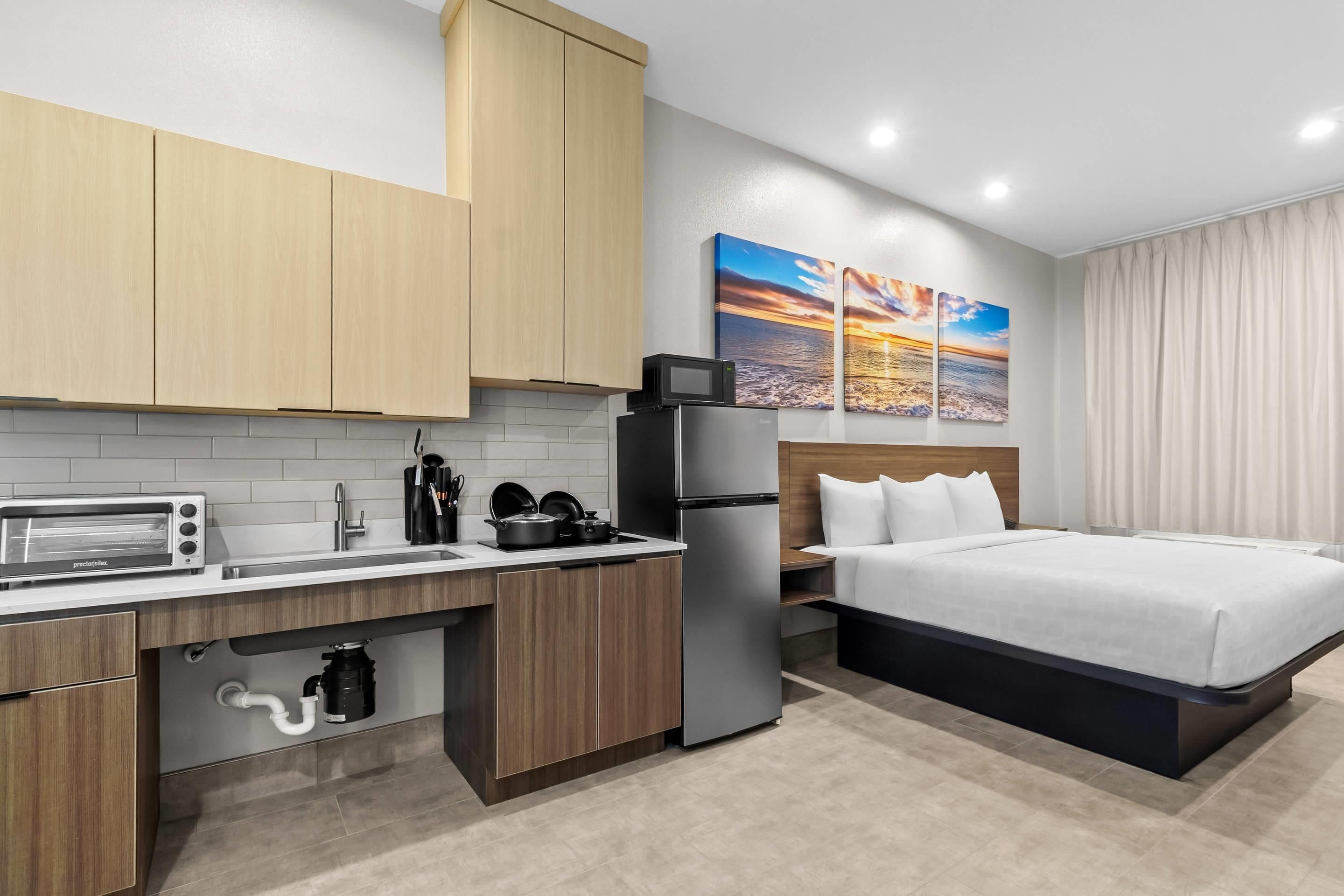 Habitación de hotel pequeña con kitchenette, una cama y un cuadro de un atardecer.