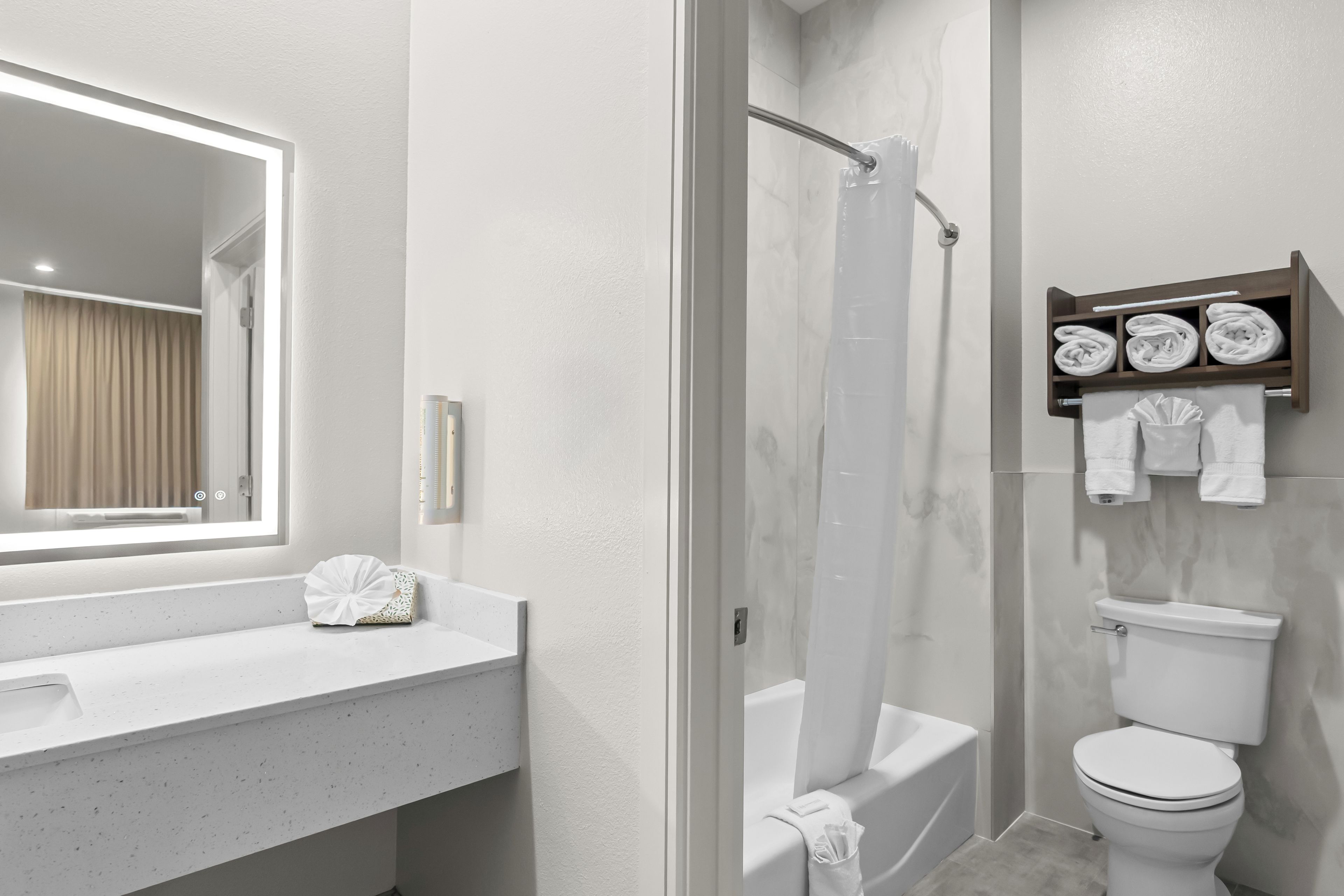 A modern bathroom with a white vanity, a glass shower enclosure, a toilet, and a towel rack with neatly folded towels.