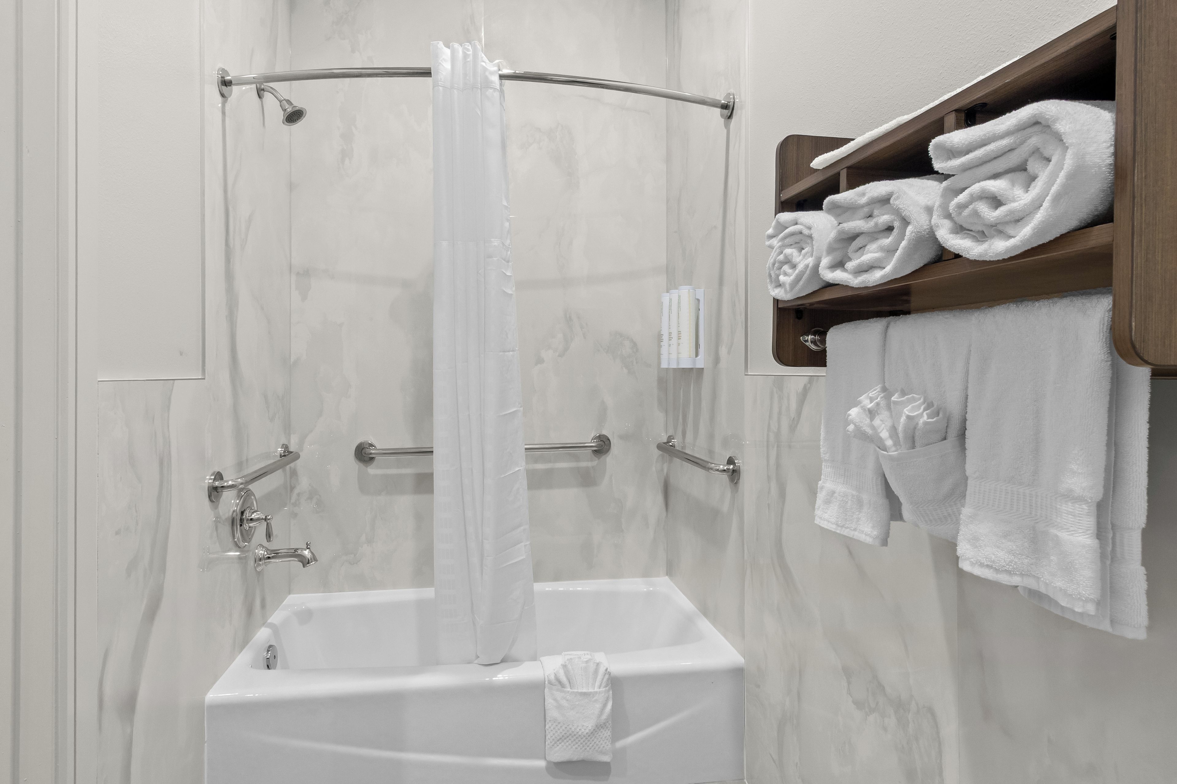 Eine Dusche mit Glastür, einer Handbrause und einem Handtuchhalter mit gefalteten Handtüchern.