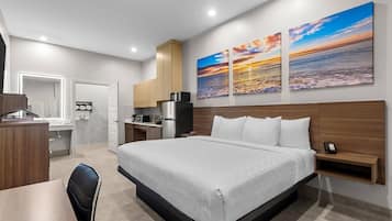 Una habitación de hotel moderna con cama, escritorio y kitchenette. Hay tres cuadros en la pared.