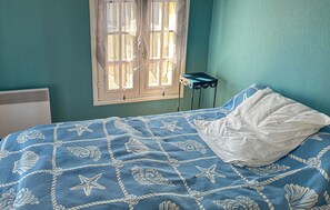 Een slaapkamer met een bed, een raam met gordijnen, een radiator en een klein tafeltje.