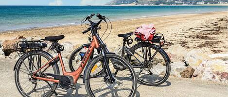 Two bicycles parked on a sandy beach with a clear view of the ocean and distant hills.