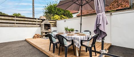 En terrasse med træterrasse, et bord dækket til fire personer og en pizzoven.