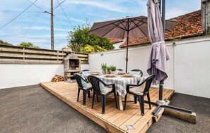 A patio with a wooden deck, a table set for four, and a pizza oven. - MAISON PROCHE DE LA MER 1 (Bricqueville sur mer)