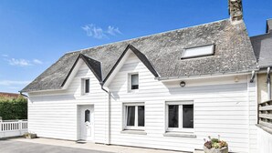 Ein weißes, zweistöckiges Haus mit Satteldach, Schornstein und einer kleinen Veranda.