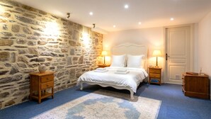 Een slaapkamer met een stenen muur, een bed met witte lakens, twee nachtkastjes met lampen en een blauw vloerkleed.