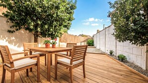 Een terras van hout, met een tafel en stoelen, omringd door een bakstenen muur en groen.