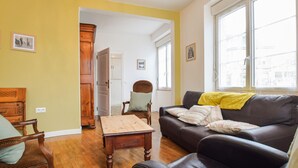 Een woonkamer met een houten tafel, een leren bank en een raam met uitzicht op gebouwen.