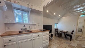 Une cuisine avec des armoires blanches, un plan de travail en bois et un évier. On y trouve également un coin repas avec une table et des chaises.