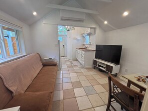 Een ruimtelijke woonkamer met een bank, een televisie, een eettafel en een keukenhoek.