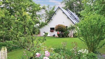 Et hvidt hus med skråtag, omgivet af en velplejet have med mange blomstrende planter og græsplæne.