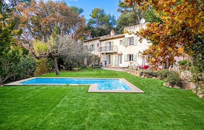 Ein zweigeschossiges Haus mit Swimmingpool, gepflegtem Rasen und umliegenden Bäumen.