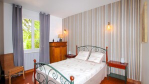 Een slaapkamer met een bed, een stoel, een kaptafel en een raam met gordijnen.