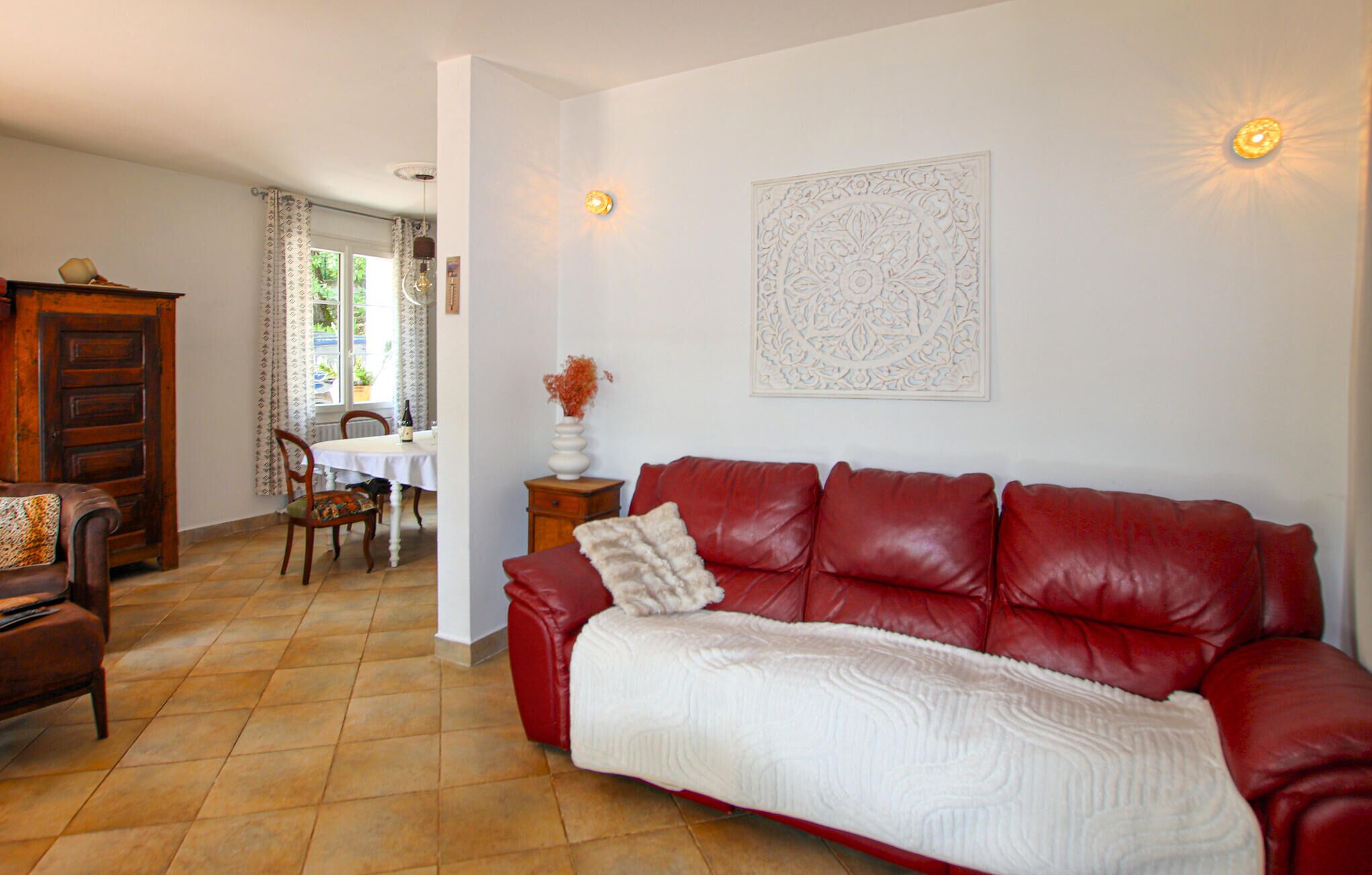 Una sala de estar con un sofá de cuero rojo, una mesa de comedor con sillas, un mueble de madera y un adorno en la pared.