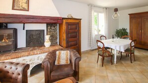 Een gezellige woonkamer met een open haard, een eettafel met stoelen, en een keukenhoek.