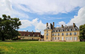 Un grand bâtiment historique, doté de nombreuses fenêtres et d’une tour, entouré d’une pelouse bien entretenue.