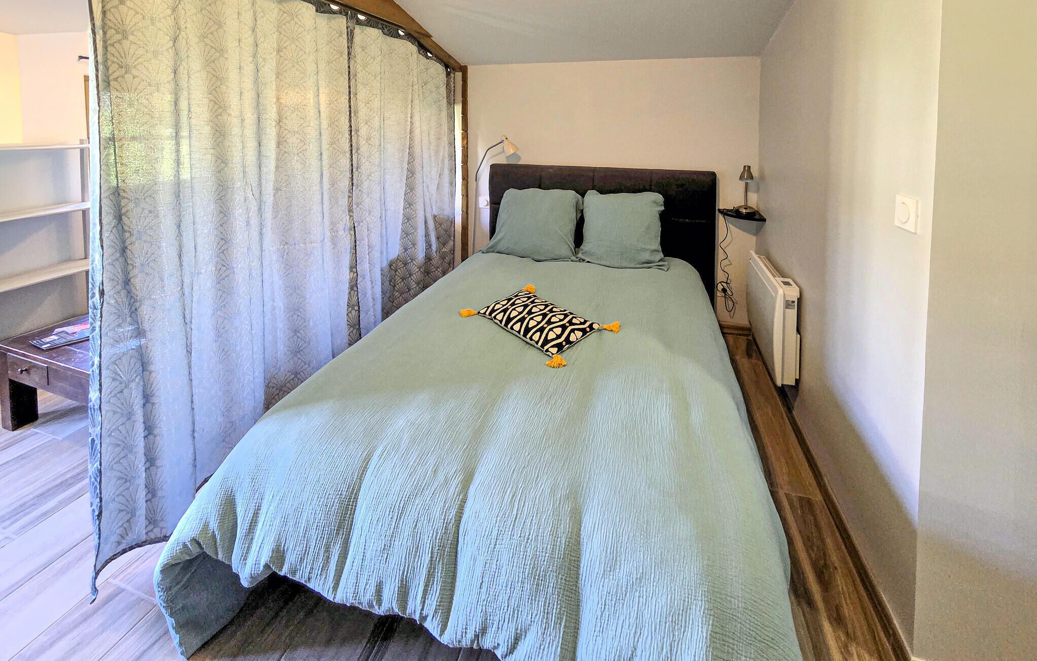 A bed with a patterned throw, two pillows, a bedside table with a lamp, and a radiator.