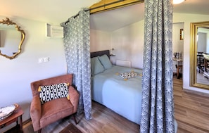A bedroom with a bed, a chair, a mirror, and a curtain.