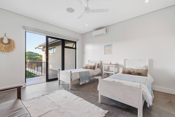 A modern bedroom with two beds, a ceiling fan, and a large sliding glass door leading to a balcony. - Room-yellow-tail Room - Staynest Guestho (Ballito)