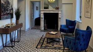 A living room with a fireplace, blue armchairs, a coffee table, a chandelier, and a patterned floor.